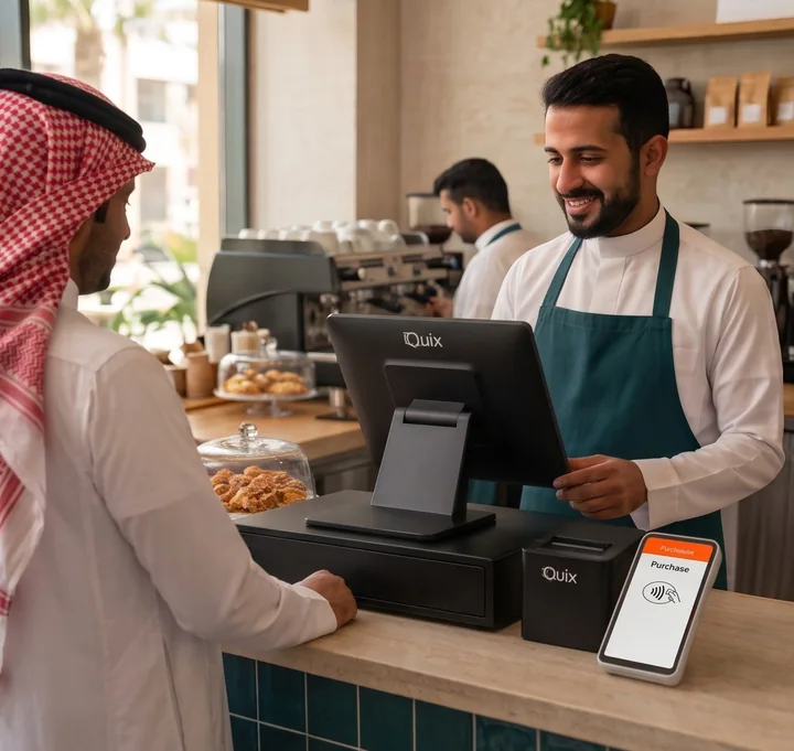 كاشير يبتسم لعميل عند منضدة مقهى، وأمامه جهاز نقطة بيع وطابعة إيصالات وجهاز دفع بالبطاقة.